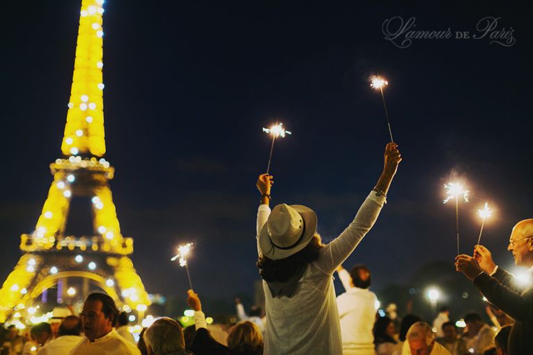 Diner en Blanc, also known as Diner in White, a top secret invitiation-only flash mob in Paris, France where 11,000 people dressed entirely in white clothes spontaneously set up tables and chairs in front of historic landmarks one night a year. The 2013 Diner en blanc, held on July 13, took place in the Louvre courtyard and by the Trocadero fountains in front of the Eiffel Tower.  Photographed by Paris wedding and portrait photographer Stacy Reeves for vacation planning blog L'Amour de Paris.