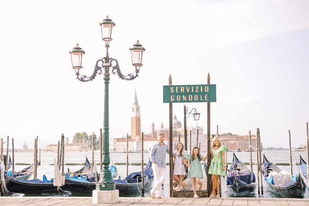 family of four taking a family portrait in front of gondolas in venice