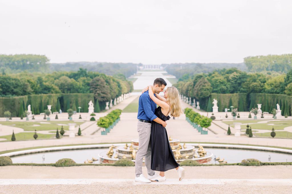 Happy couple embracing after surprise proposal in front of Versailles palace