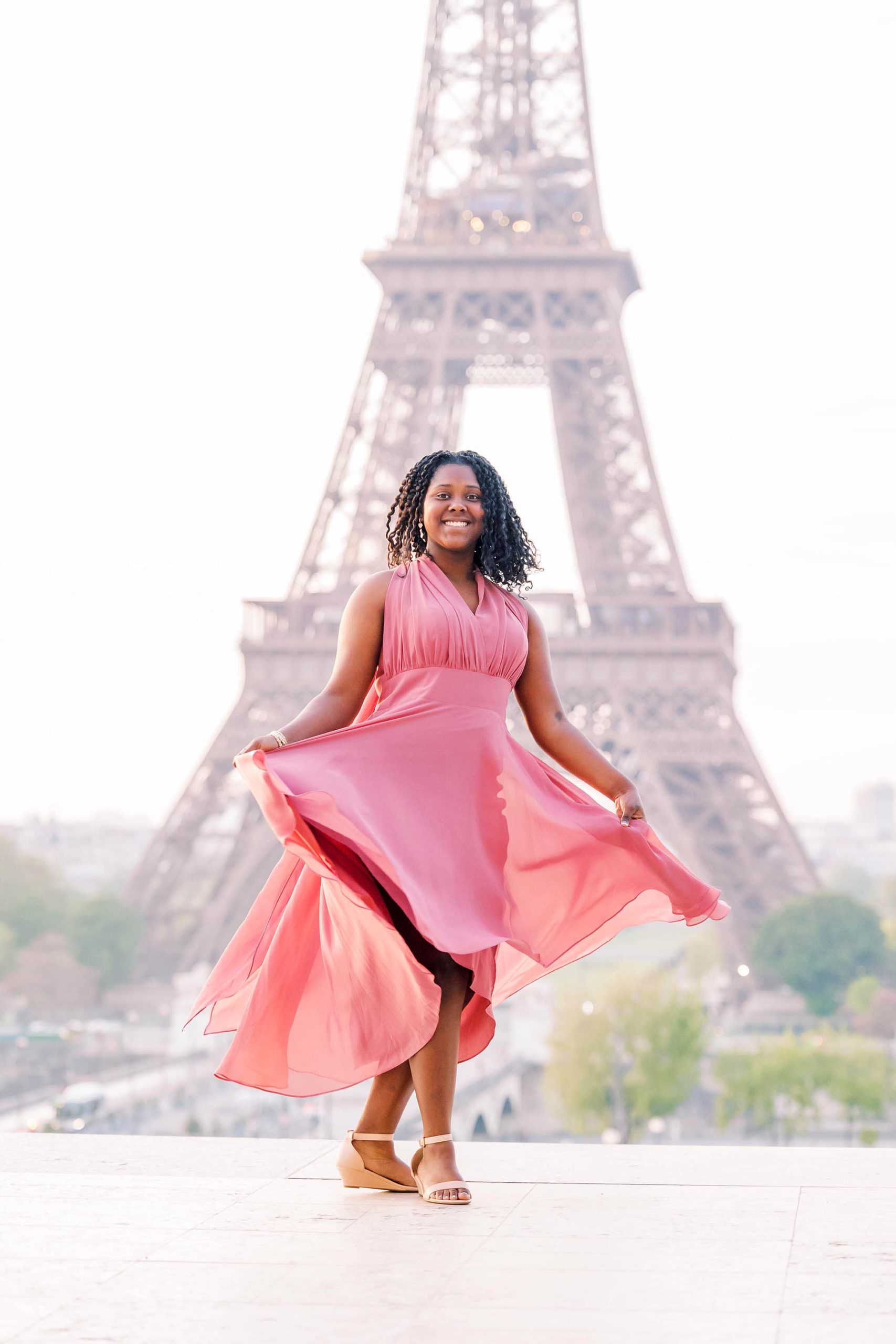Joyful young Black girl smiling in front of the Eiffel Tower during her Paris portrait session