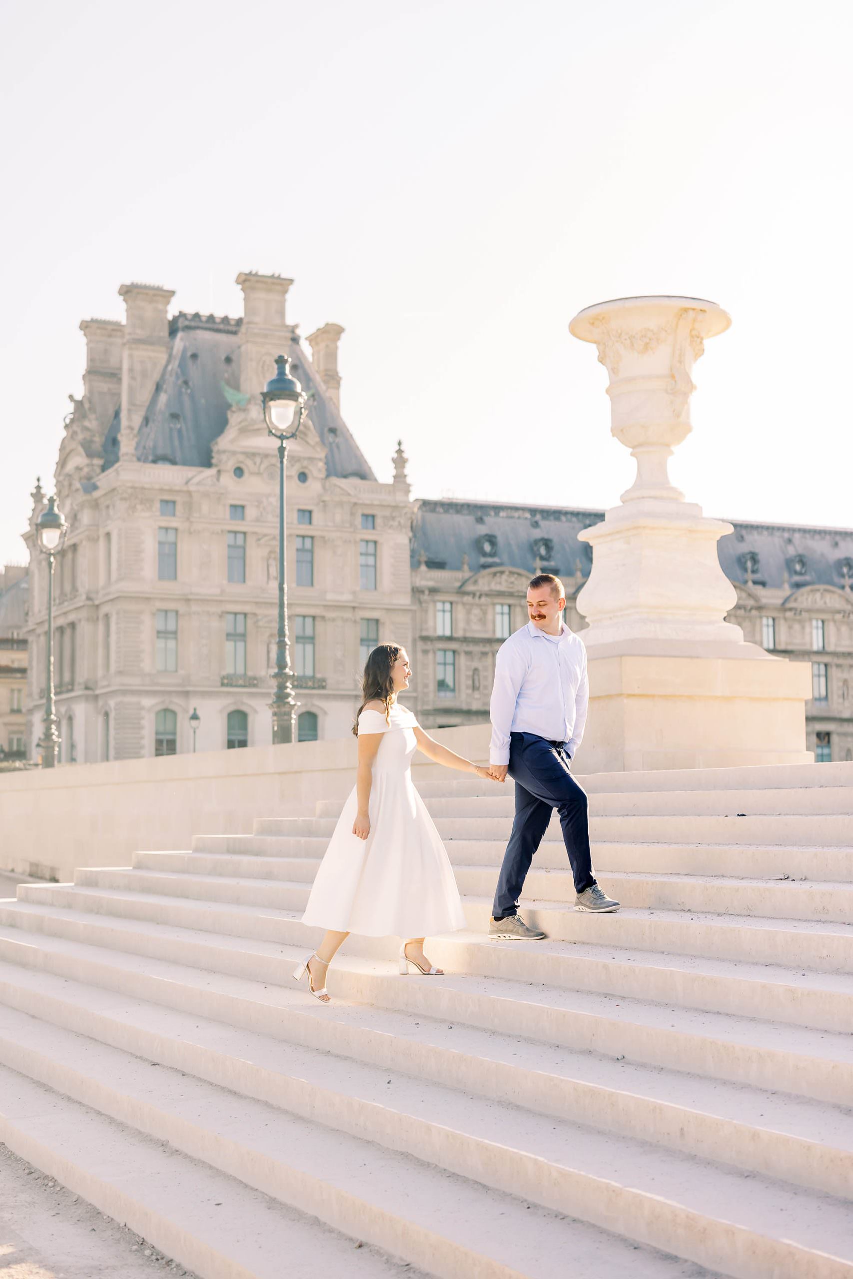 couple walking up the stairs for a portrait with the louvre in the background