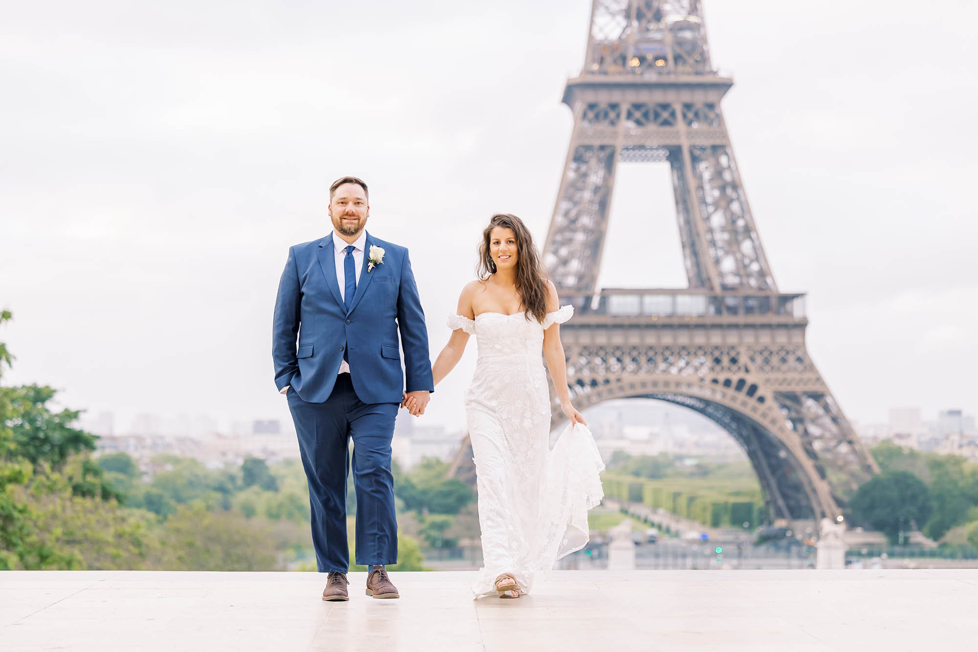 young couple in wedding attire walking in front of the eiffel tower