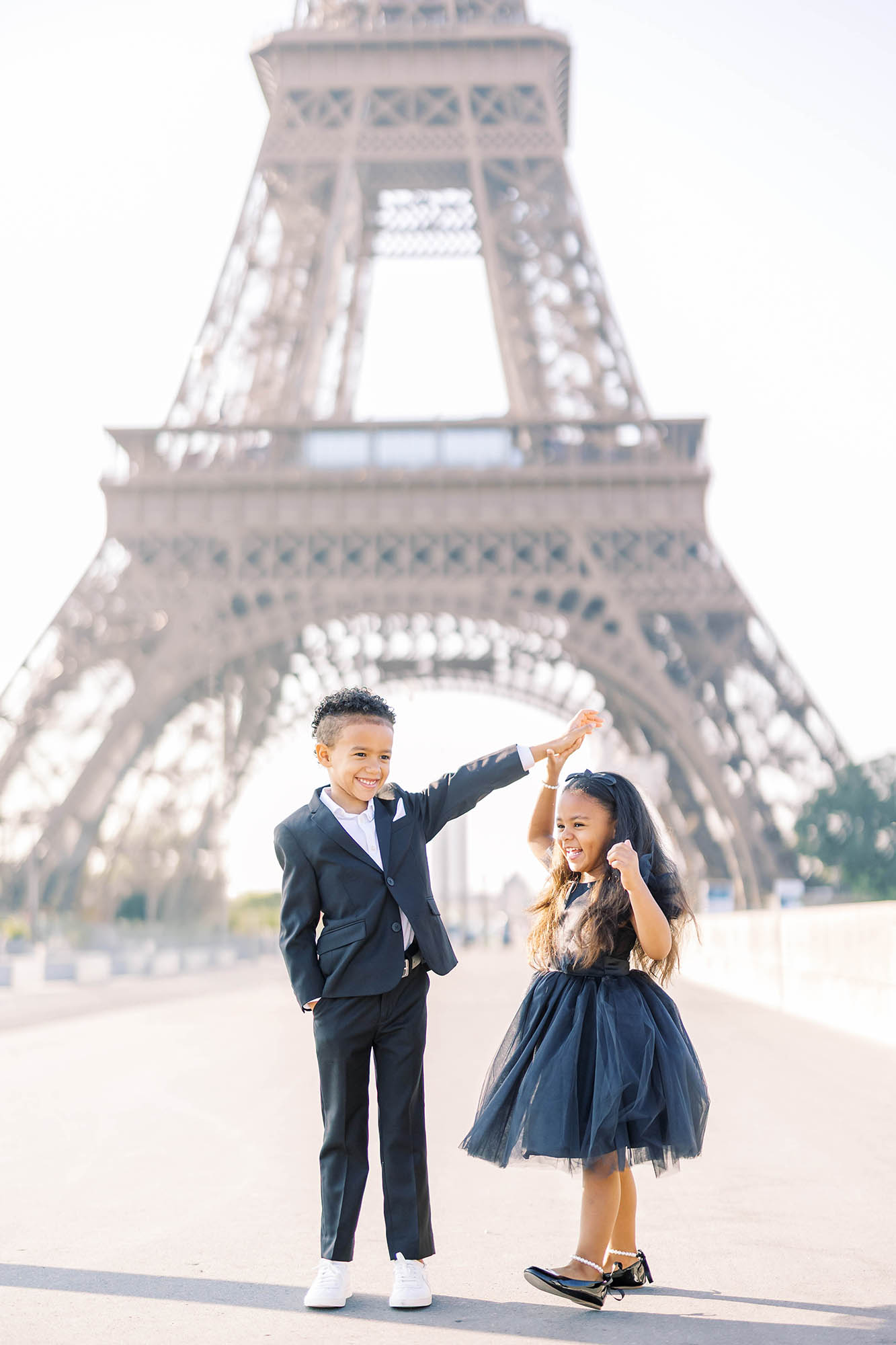 cute young brother twirling his little sister while dancing in front of the eiffel tower in paris