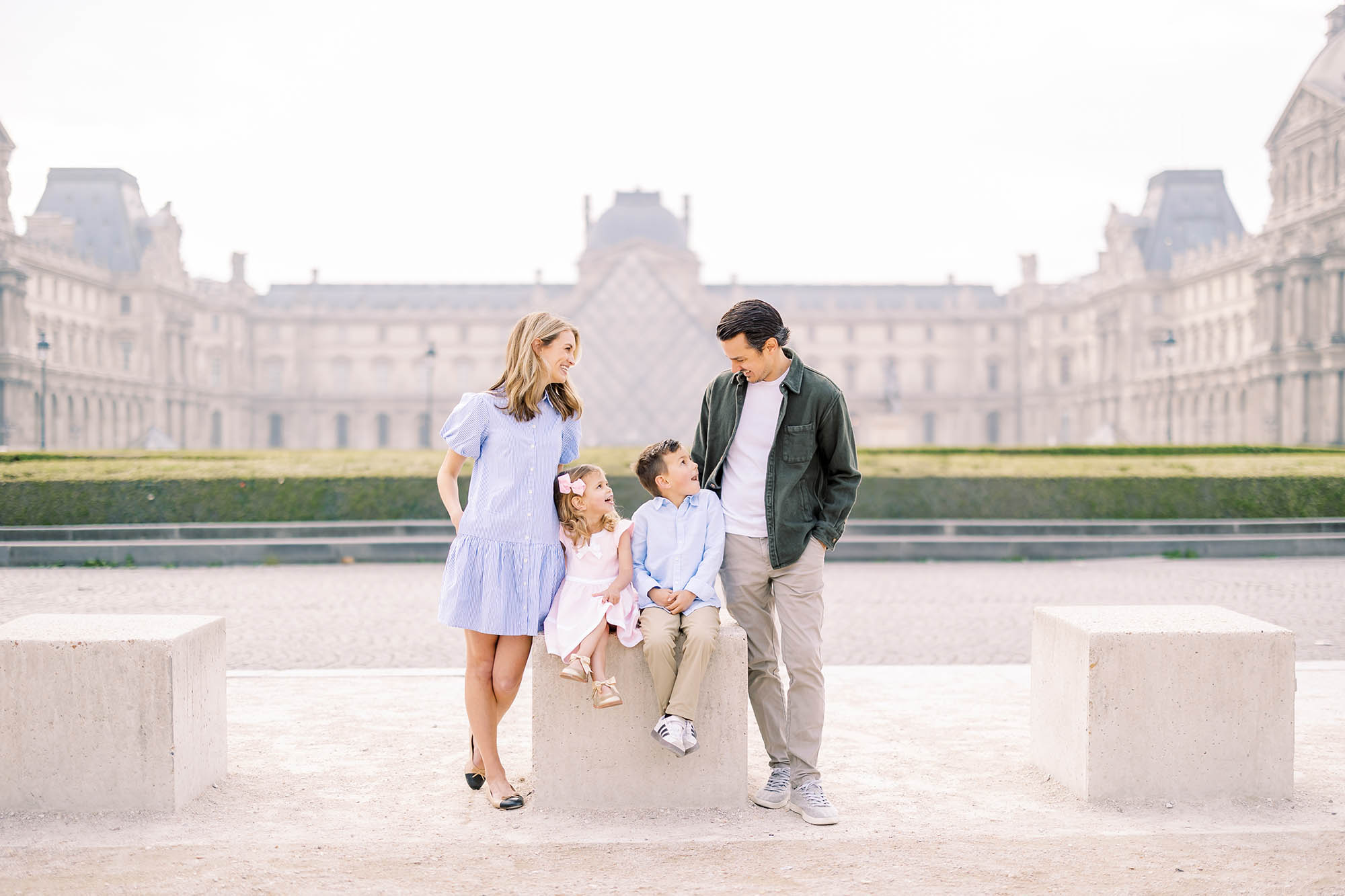 cute young family in a casual family portrait in front of the louvre in paris