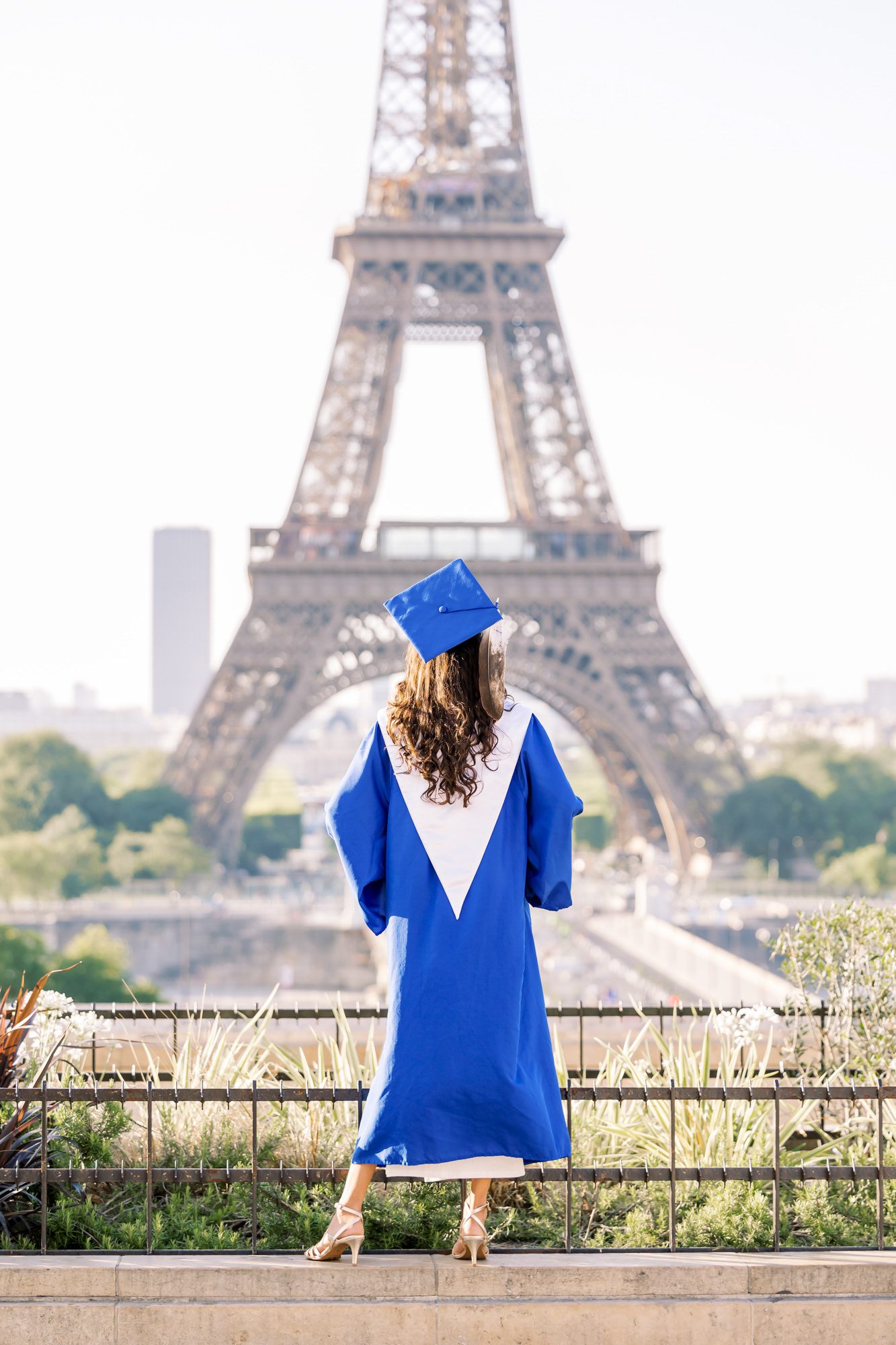 Senior girl wearing a graduation cap and gown in front of the Eiffel Tower in Paris