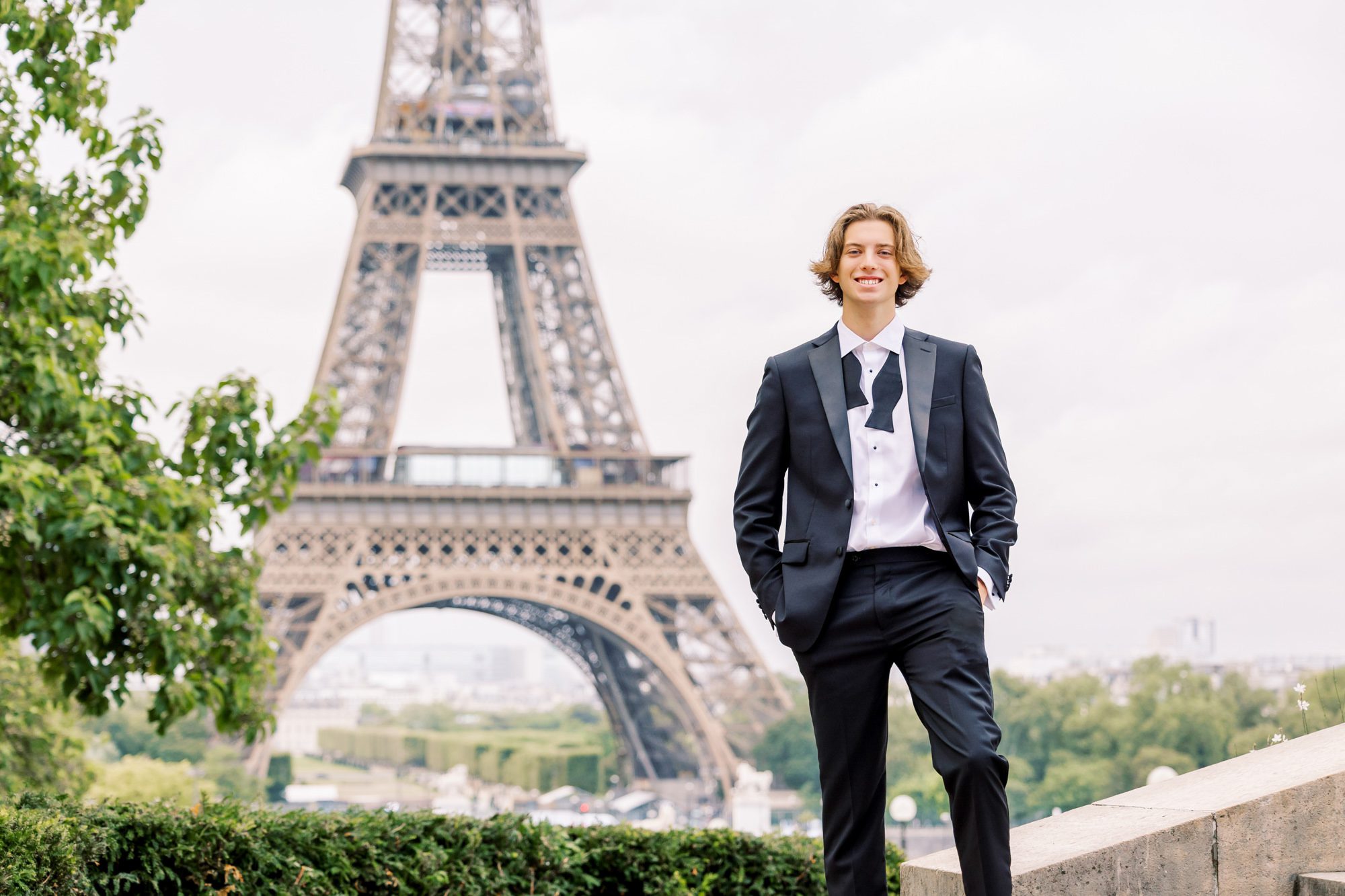 handsome guy in a casual pose wearing a black tux for senior pics in paris at the eiffel tower