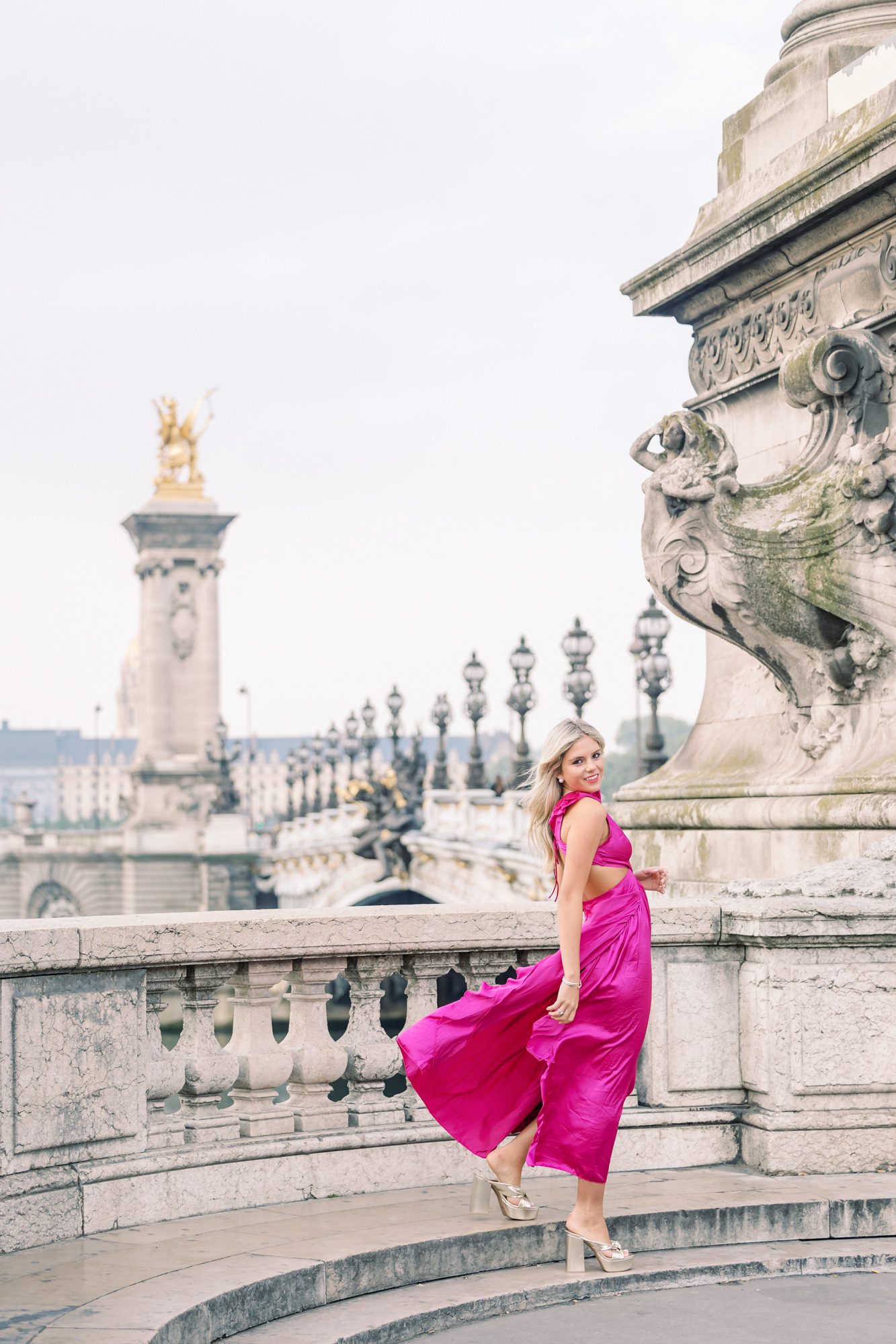 Editorial shot of a senior girl walking in a long, flowing pink dress at Pont Alexandre III in Paris