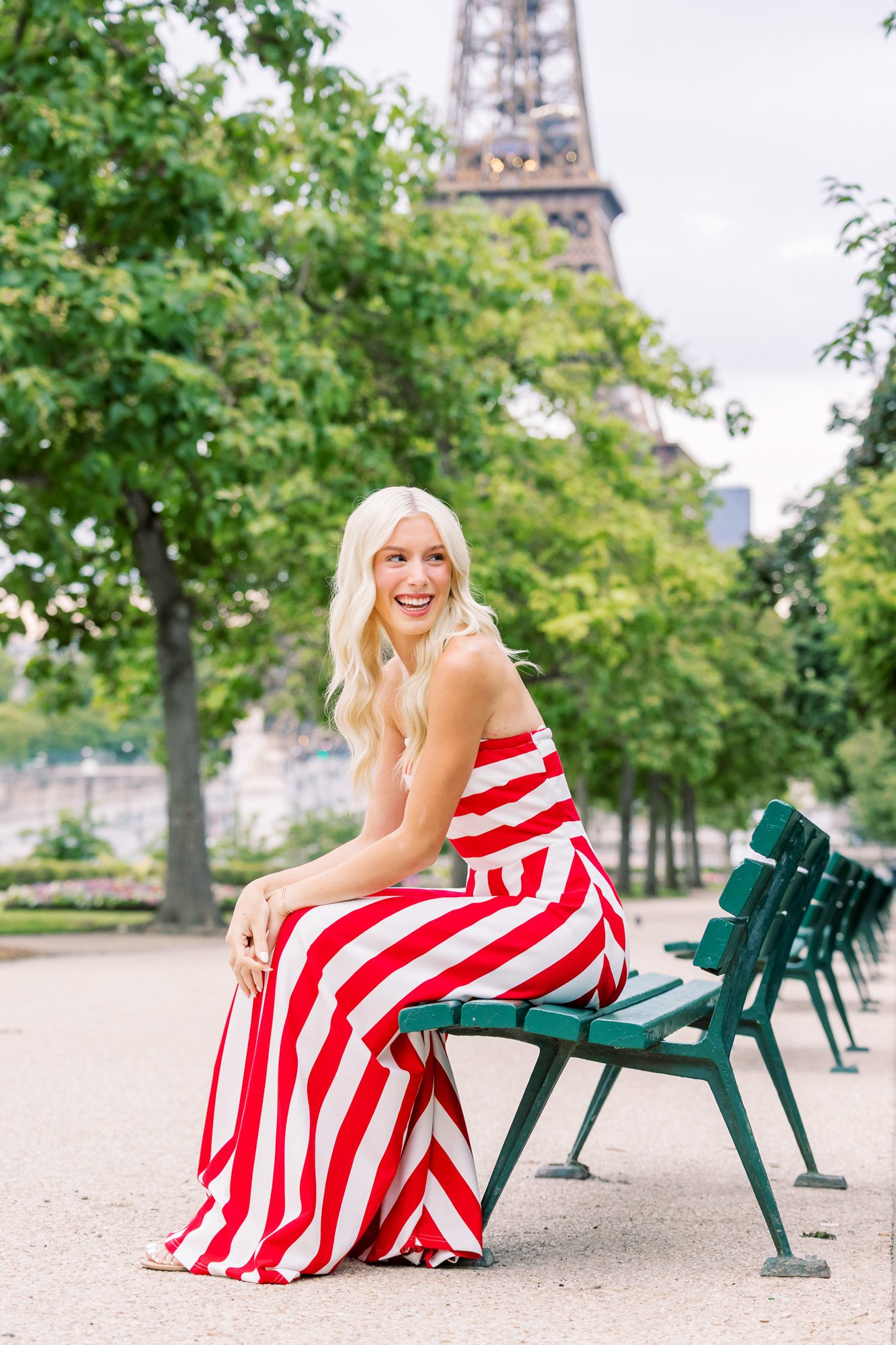 Senior girl posing on a bench for senior pics in Paris in a red and white striped dress with a view of the Eiffel Tower.