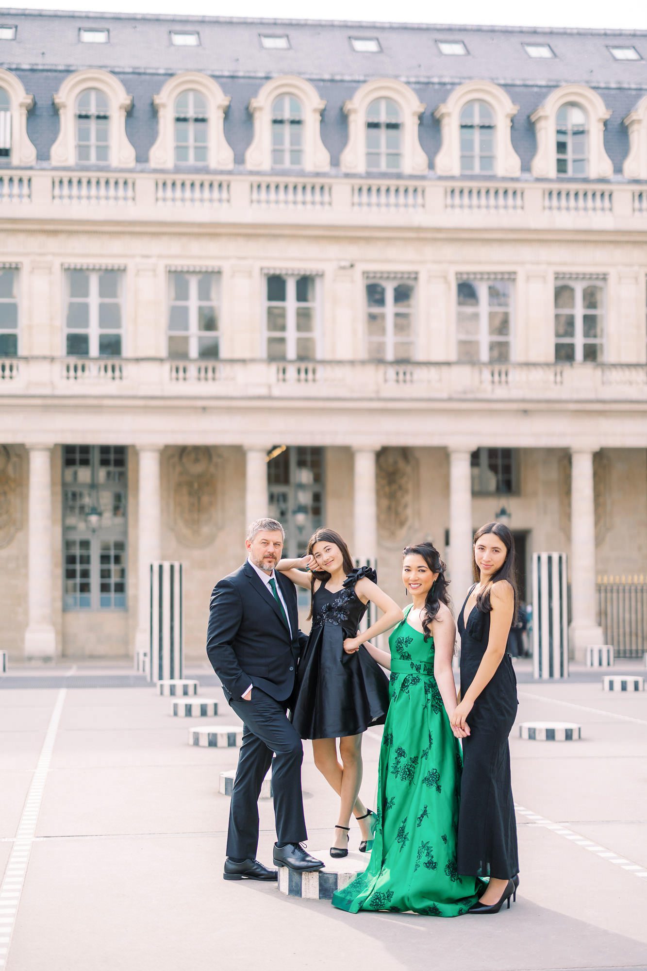 A family of four in formal evening wear posing among the Buren Columns at Palais Royal. The mother stands out in a stunning emerald green gown against the historic architecture. High-fashion family portraiture in Paris.