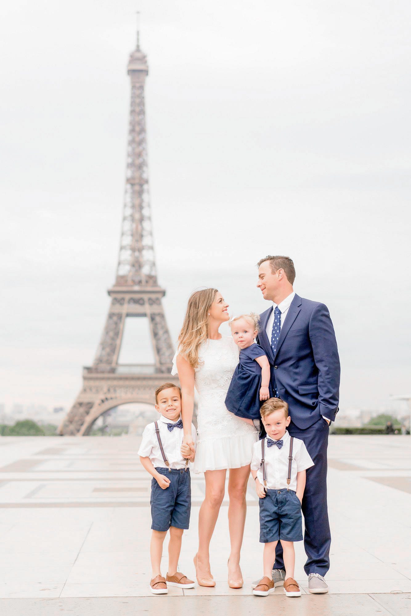 A polished family portrait of five at Trocadro with the Eiffel Tower centered in the background. The family is dressed in coordinated shades of navy blue and white, capturing a classic Parisian morning aesthetic.