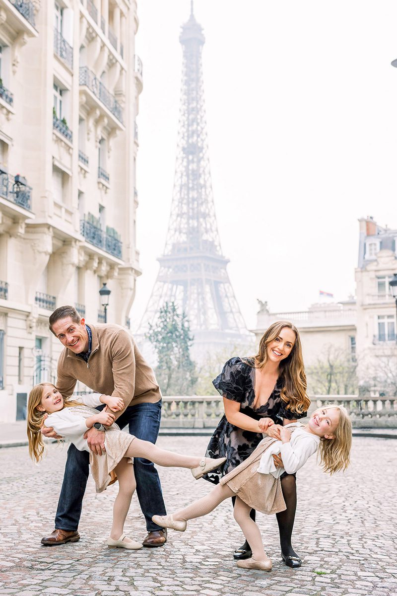 paris photographer review photo of a family of four, mom and dad are dipping young daughters in front of Eiffel Tower as they all giggle.