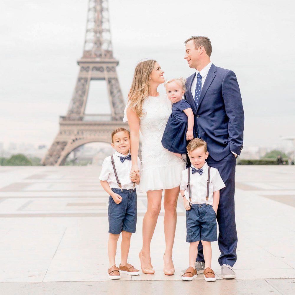 A polished family portrait of five at Trocadéro with the Eiffel Tower centered in the background. The family is dressed in coordinated shades of navy blue and white, capturing a classic Parisian morning aesthetic.