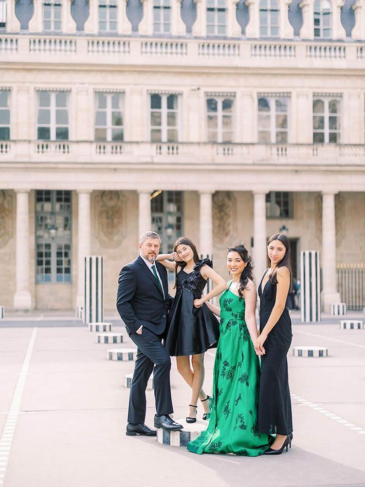 A family of four in formal evening wear posing among the Buren Columns at Palais Royal. The mother stands out in a stunning emerald green gown against the historic architecture. High-fashion family portraiture in Paris.